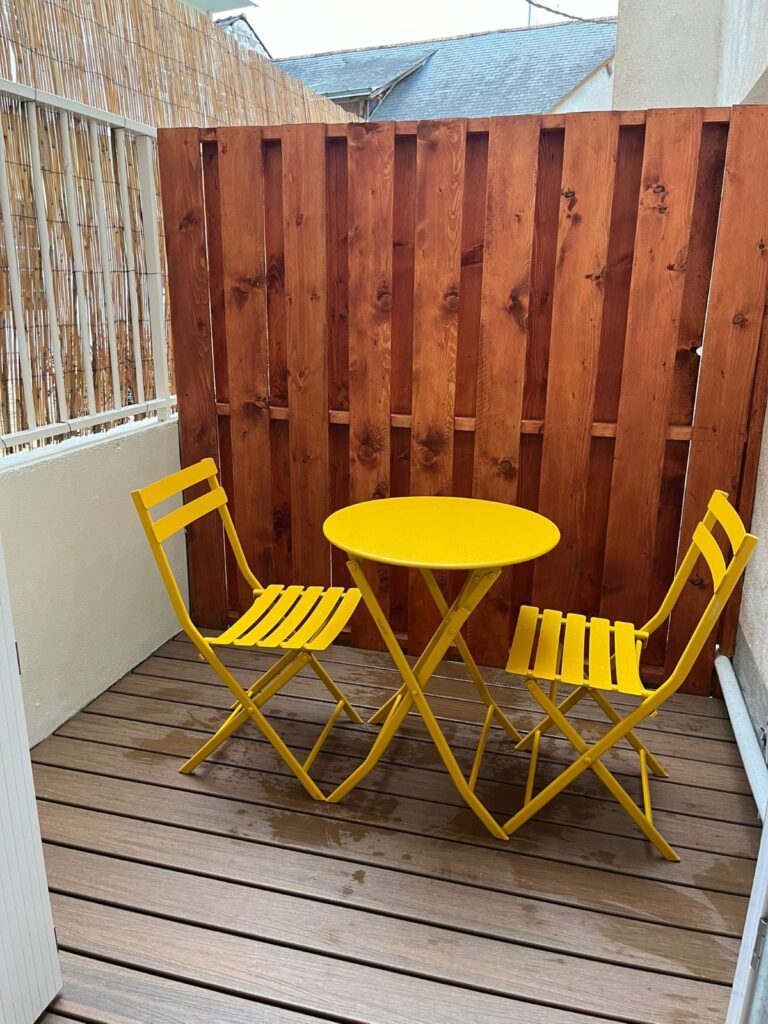 Terrasse extérieur, avec table ronde et deux chaises jaunes.