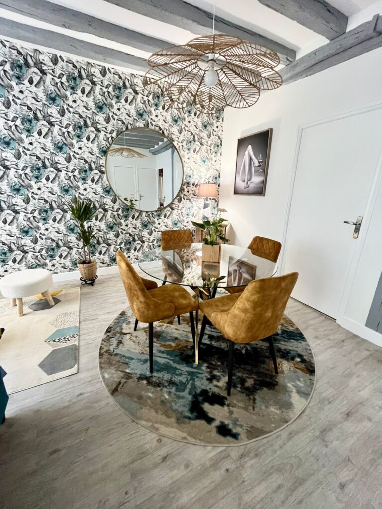 Salle à manger contemporaine avec table ronde en verre, chaises en velours ocre et miroir rond mural.